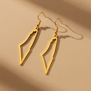 Deux boucles d’oreilles dorées en forme de Palestine posées à plat sur fond beige